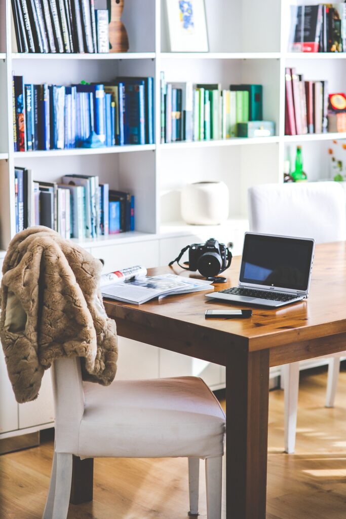 A thoughtful individual reading a book at a desk with a laptop and notepad nearby.