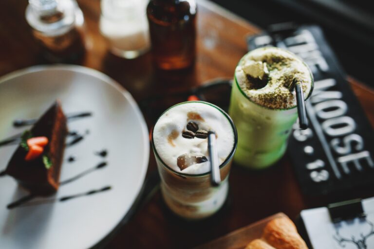 A cup of frothy matcha green tea latte with a bamboo whisk and tea leaves.